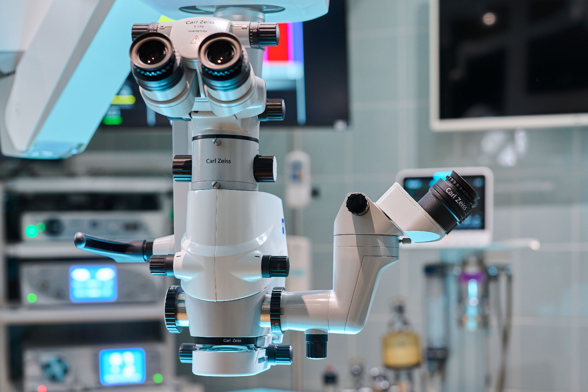 Eine Nahaufnahme eines Operationsmikroskops in einem Operationssaal. Sie zeigt mehrere Okulare und Steuerarme, im Hintergrund sind medizinische Geräte sichtbar.